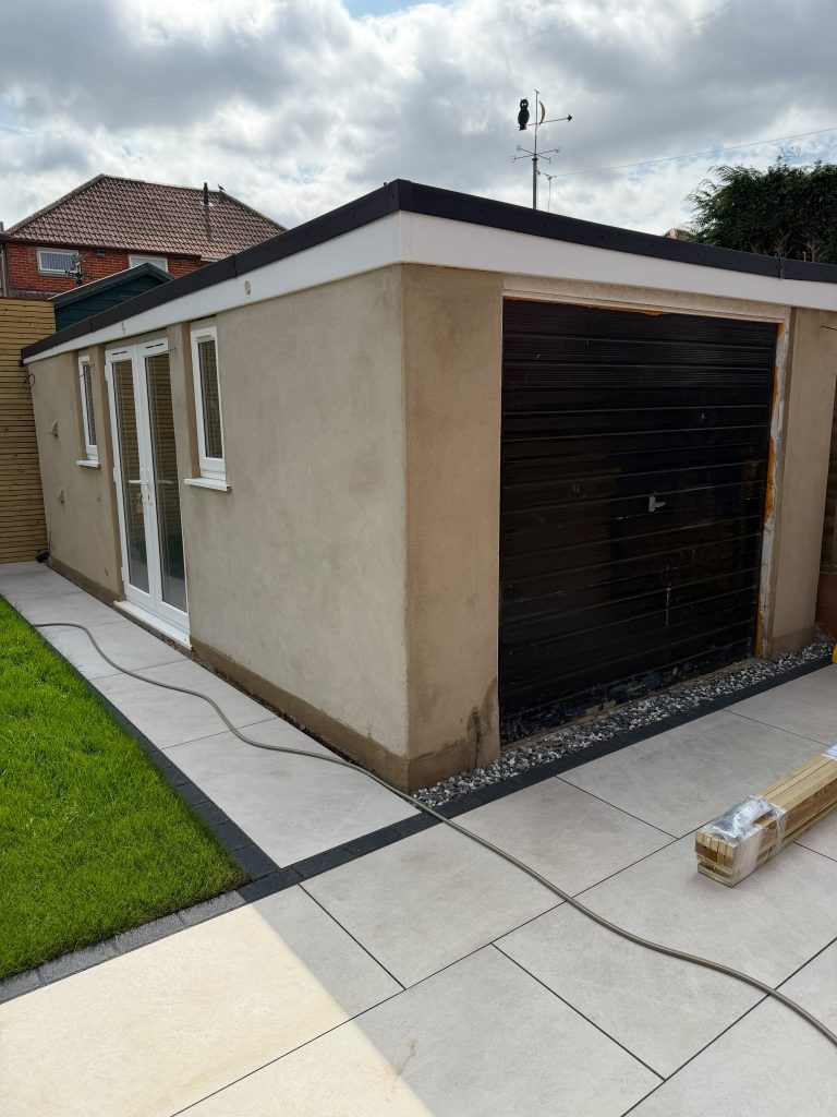 Exterior of a rendered garage in Southampton before painting, showing weathered beige walls, white uPVC doors and a black roller garage door.